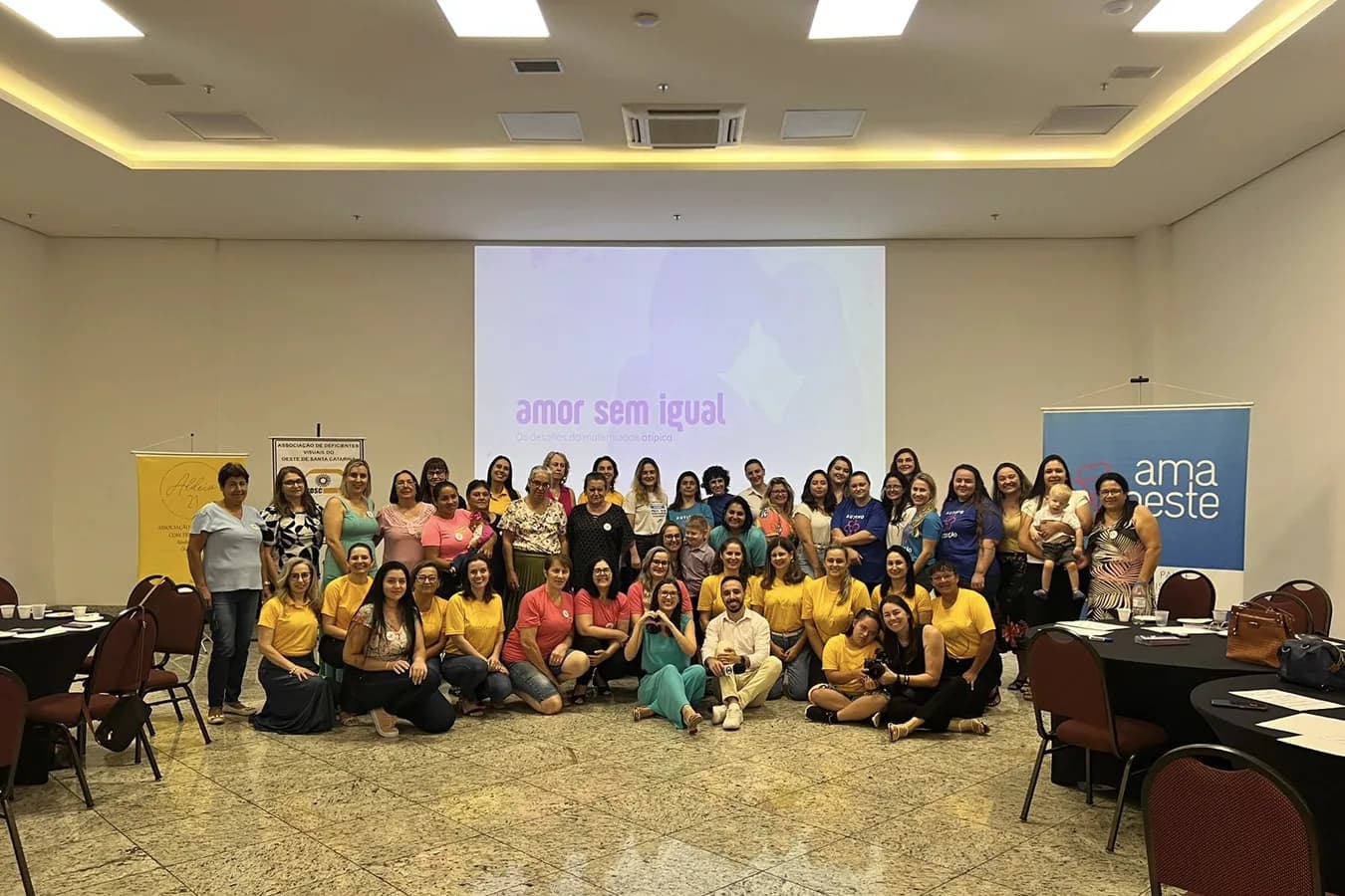 Grupo grande de participantes reunido para uma foto em frente ao telão, em um salão de eventos.