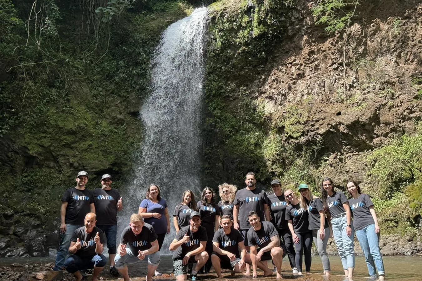 Grupo de pessoas de camiseta preta em frente a uma cachoeira.